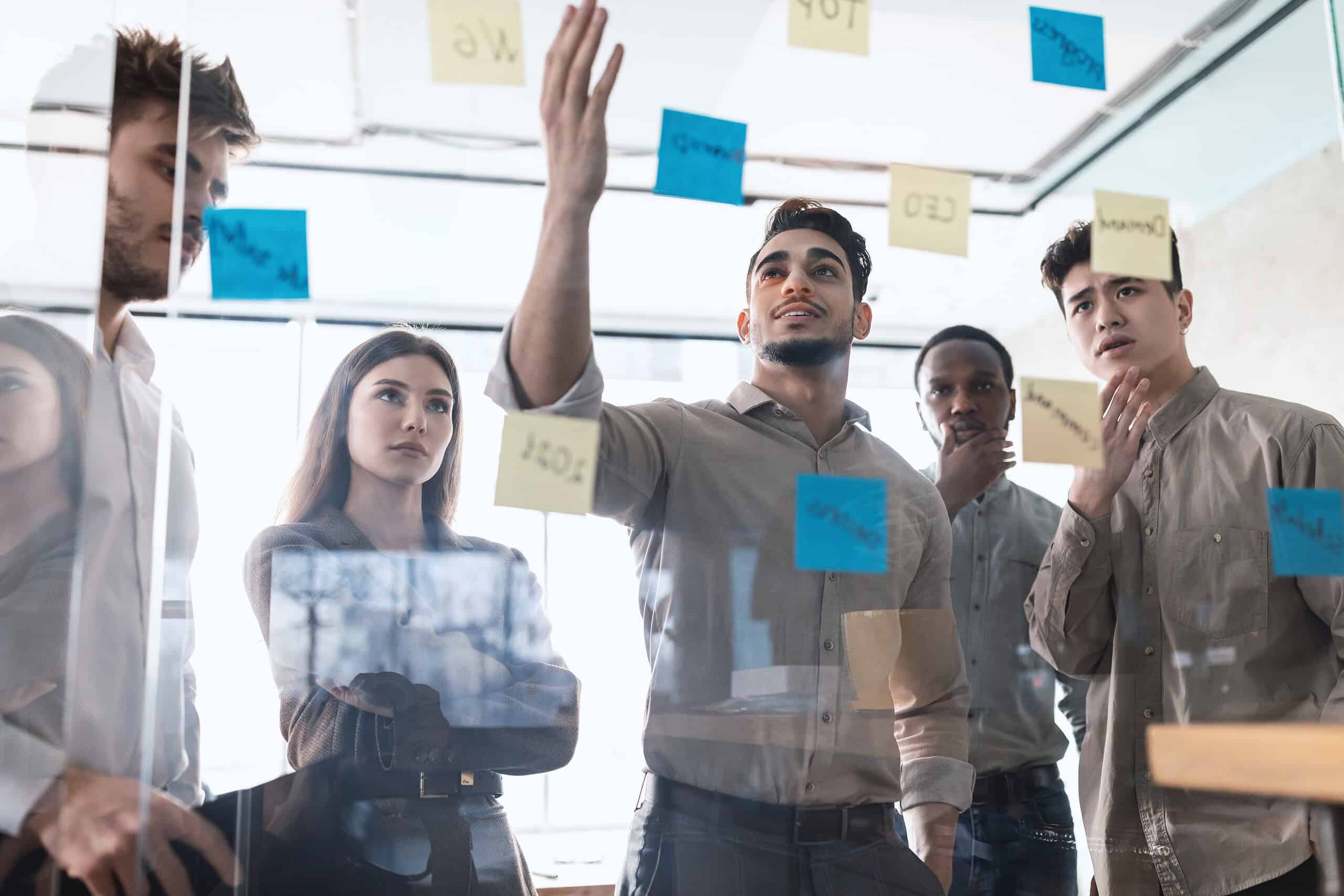 diverse colleagues brainstorming using sticky post it notes on glass wall