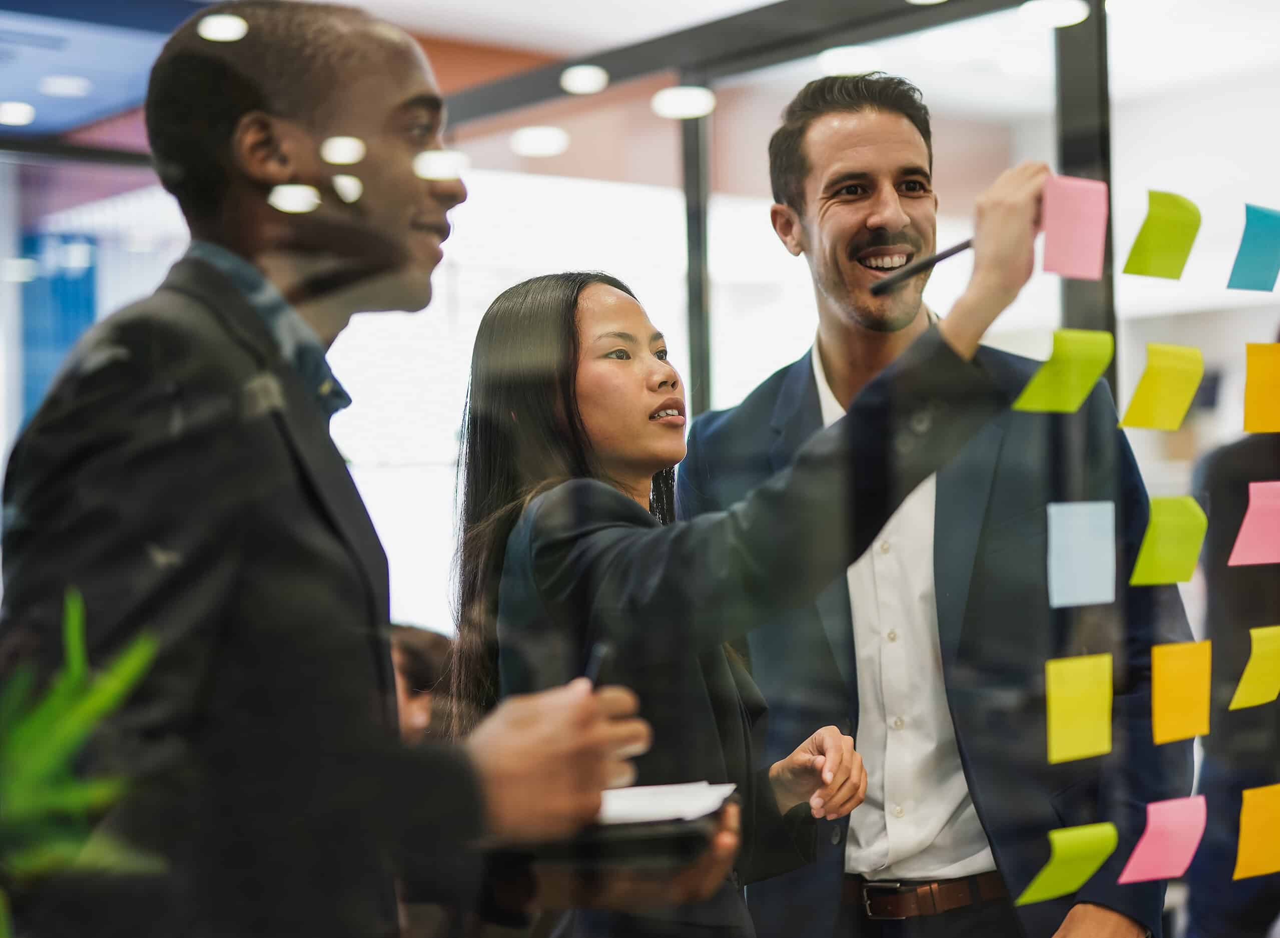 multiracial business people writing on adhesive notes stuck over glass inside modern office