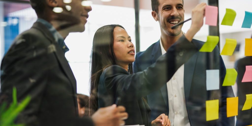 multiracial business people writing on adhesive notes stuck over glass inside modern office